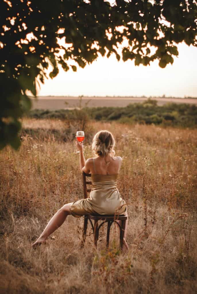 Ein Glas Rose auf einem Stuhl im Feld trinkend als Independent Escort mit Sommerkleid.