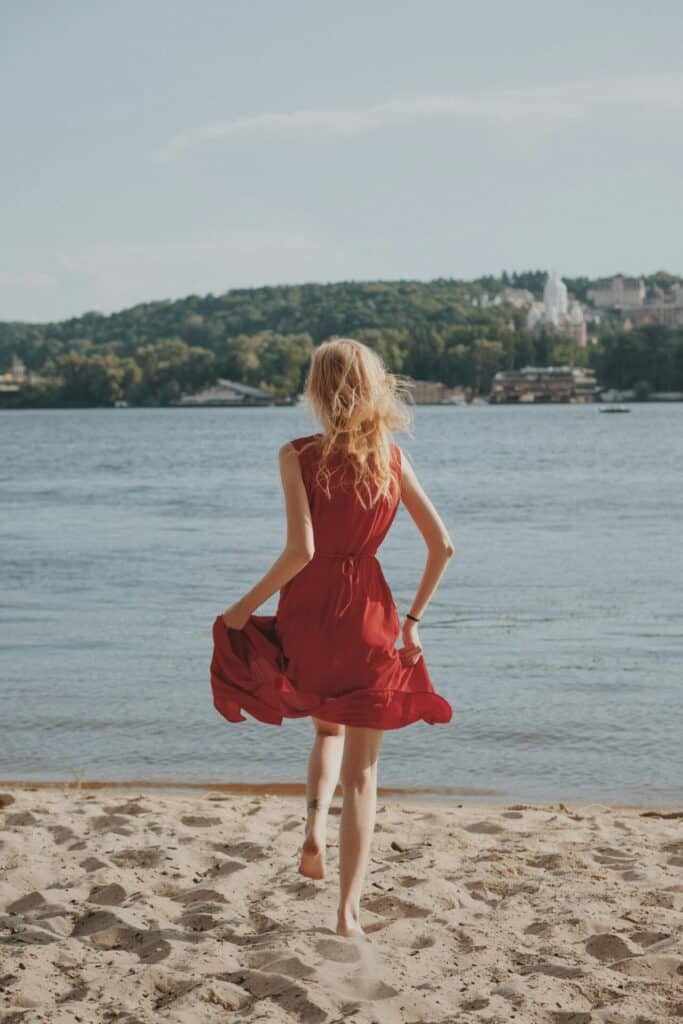 Escortgirl im roten Kleid über den Strand laufend.