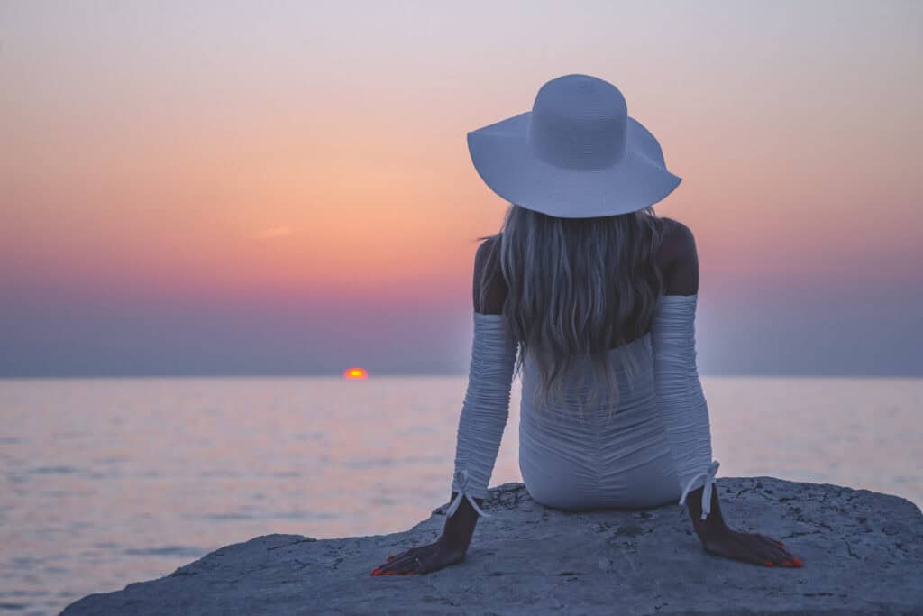 Frau im weißen Kleid am Strand den Sonnenuntergang betrachtend.